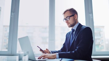 Employer reviewing sponsorship visa information on laptop and mobile device in office environment