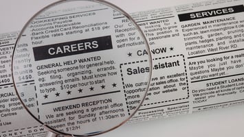 Job advertisement listings under magnifying glass representing skilled worker recruitment and labour shortages in Australia